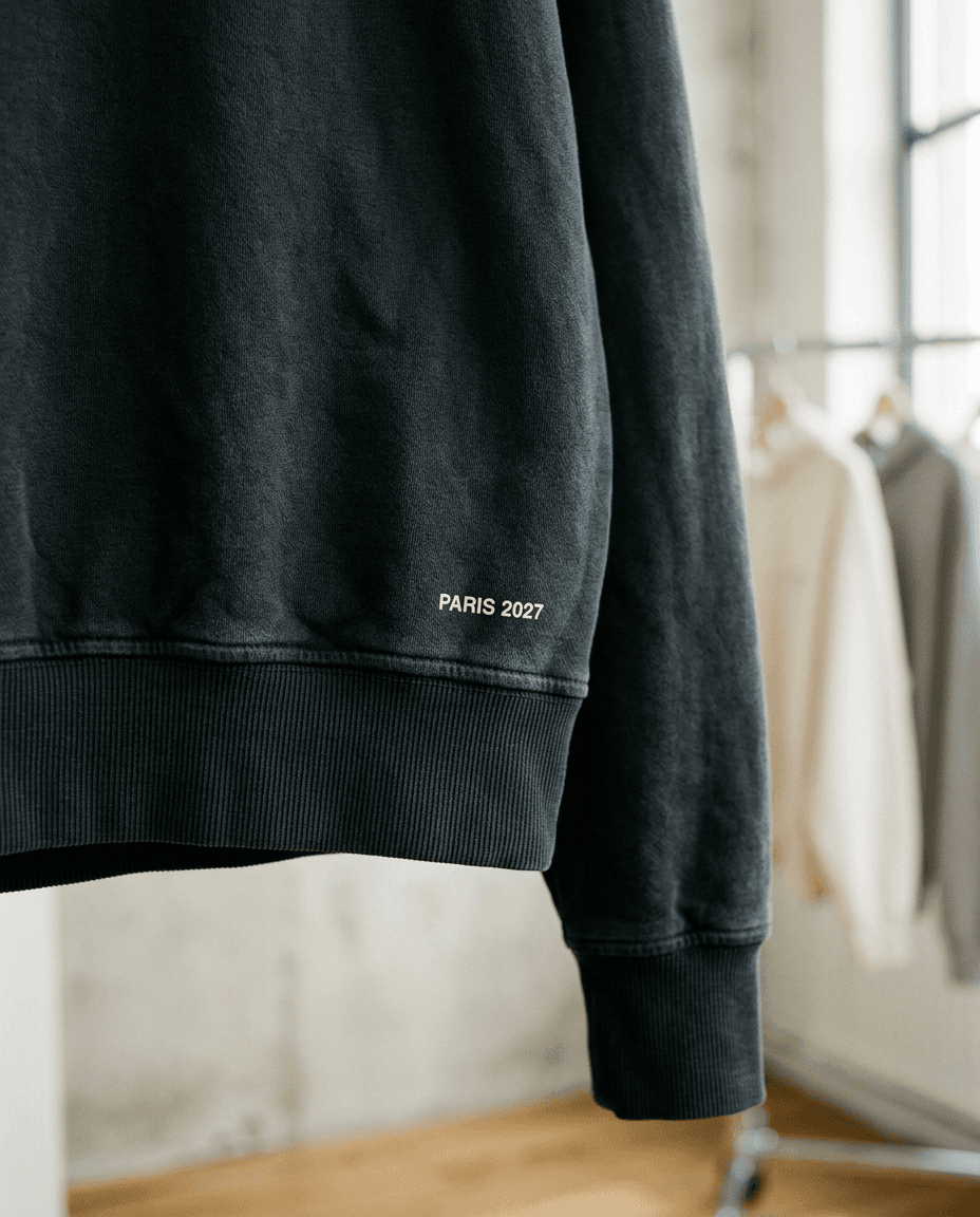Nærbillede af kanten på en hoodie med et diskret print lige over ribkanten: Paris 2027