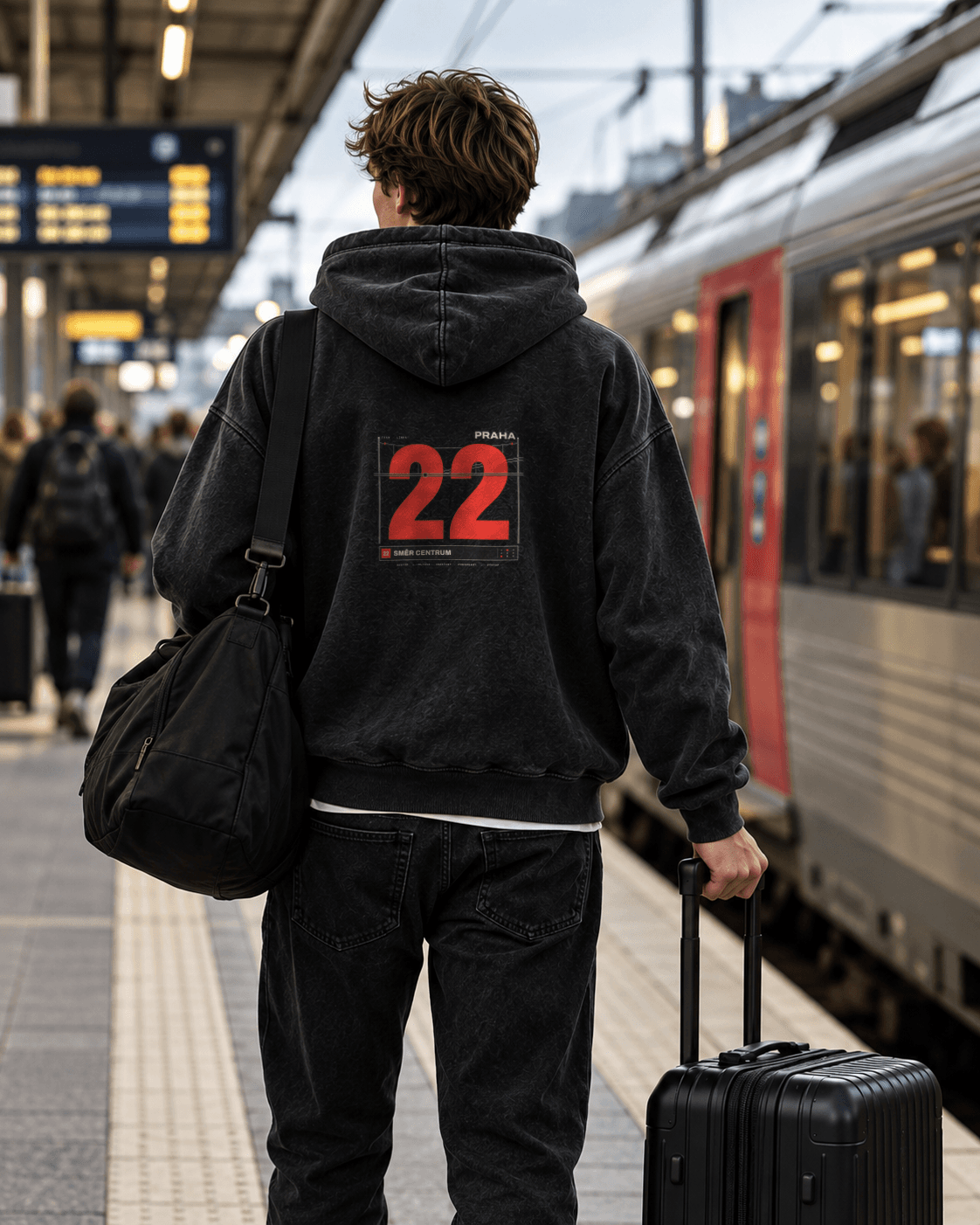 Person set bagfra på en togperron i en washed black hoodie med Praha 02 Tram 22-rygprint