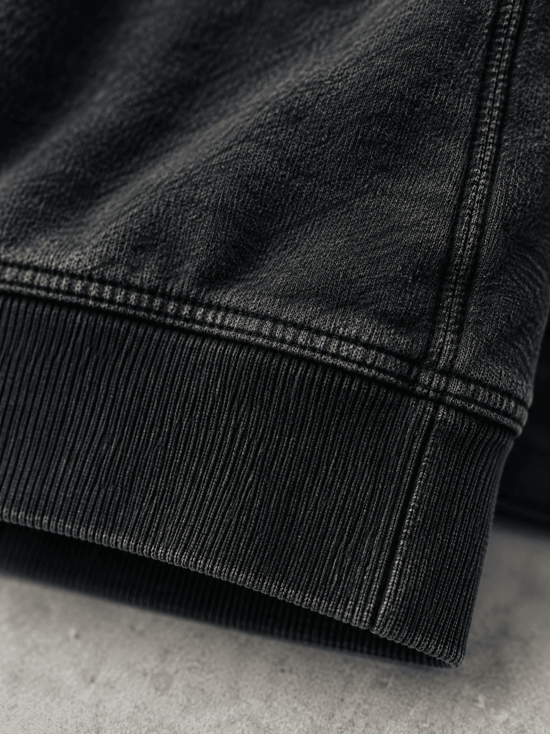 Nærbillede af ribkanten og de dobbelte sømme nederst på en washed black hoodie